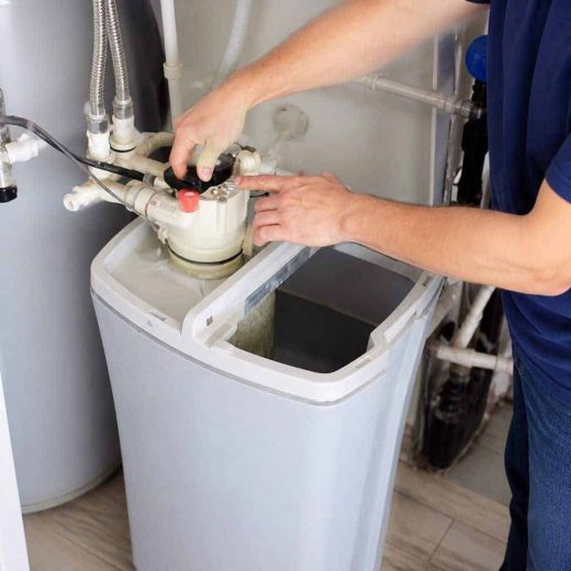 A technician in navy shirt adjusting valves and fittings on top of an open water softener unit